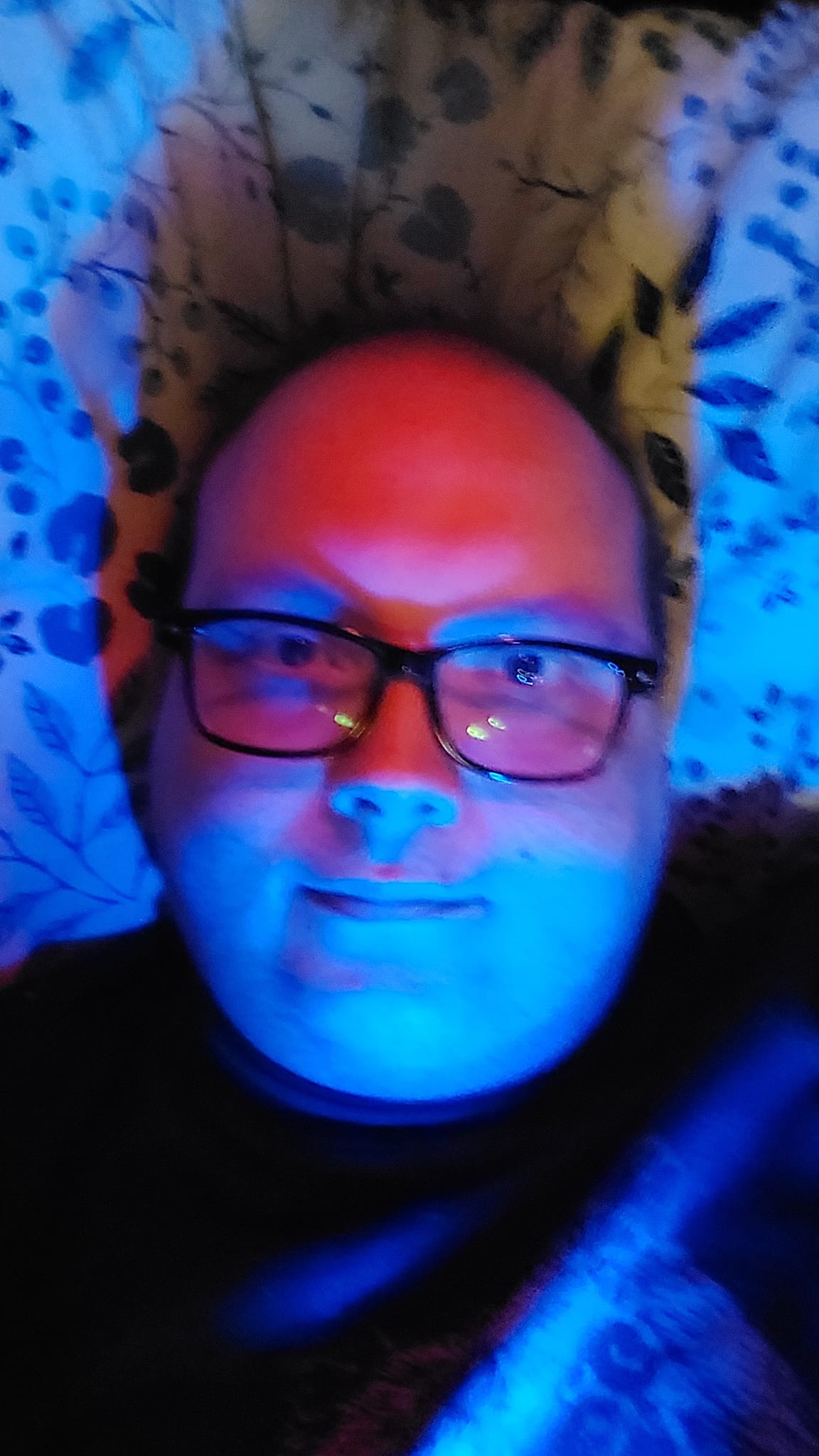 A man lays in bed, illuminated by blue light from the bottom and red light from above